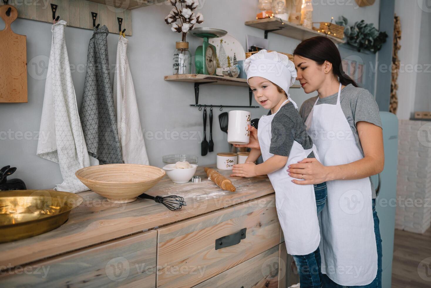 giovane contento mamma e sua bambino cucinare biscotti a casa nel il cucina. Natale fatti in casa Pan di zenzero. carino ragazzo con madre nel bianca uniforme e cappello cucinato cioccolato biscotti foto