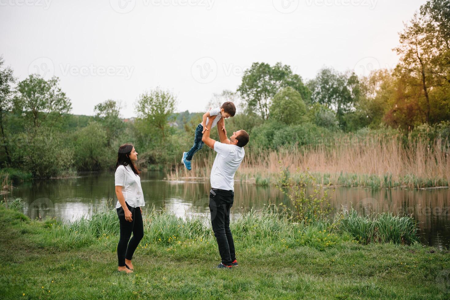 contento famiglia madre padre e bambino figlio su natura su tramonto. mamma, papà e ragazzo ridendo e abbracciare, godendo natura fuori. soleggiato giorno, bene umore. concetto di un' contento famiglia. foto