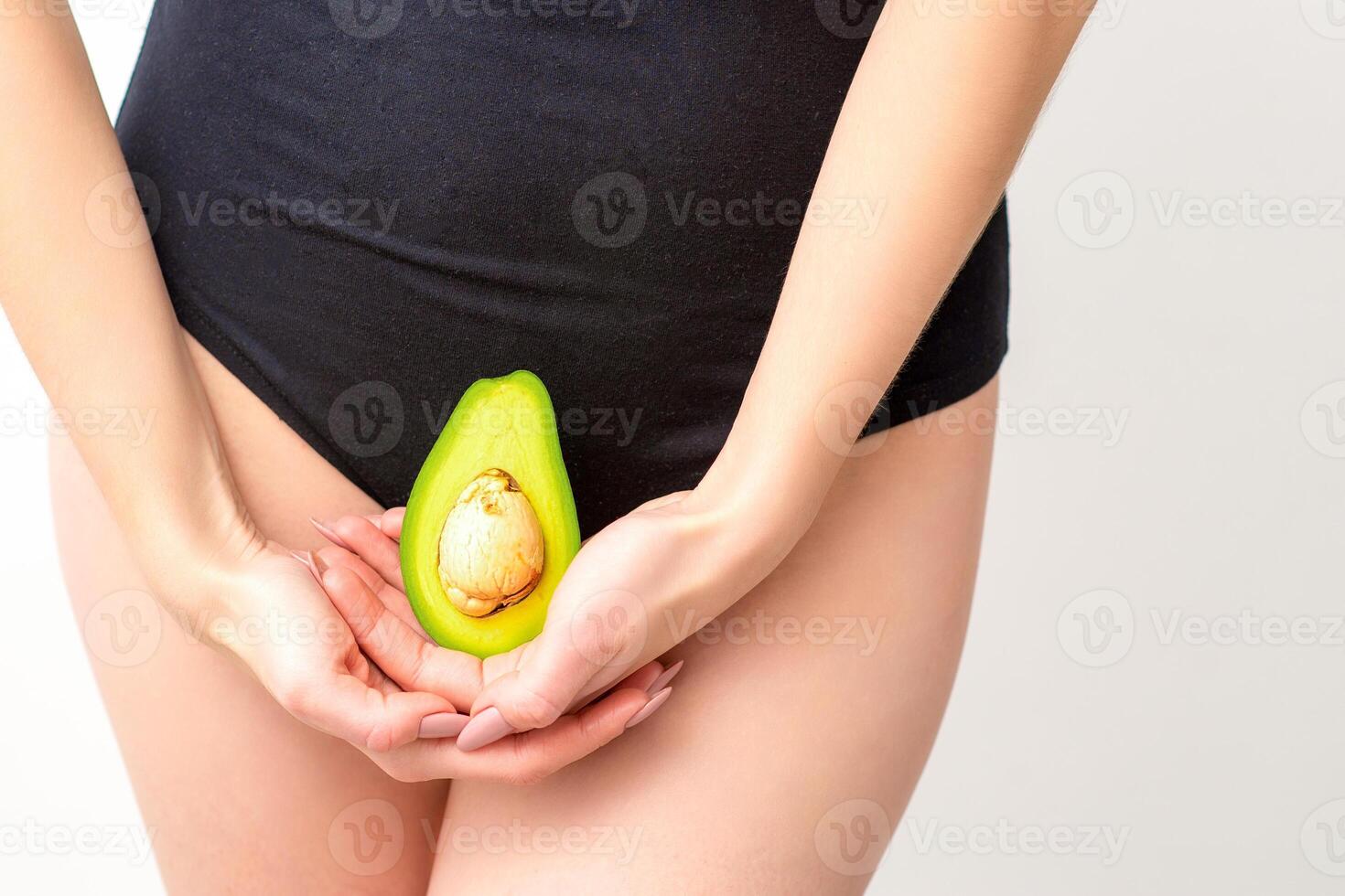 giovane donna Tenere uno metà di un' fresco avocado frutta vicino per sua pancia contro un' bianca sfondo, salutare nutrizione e gravidanza concetto. foto