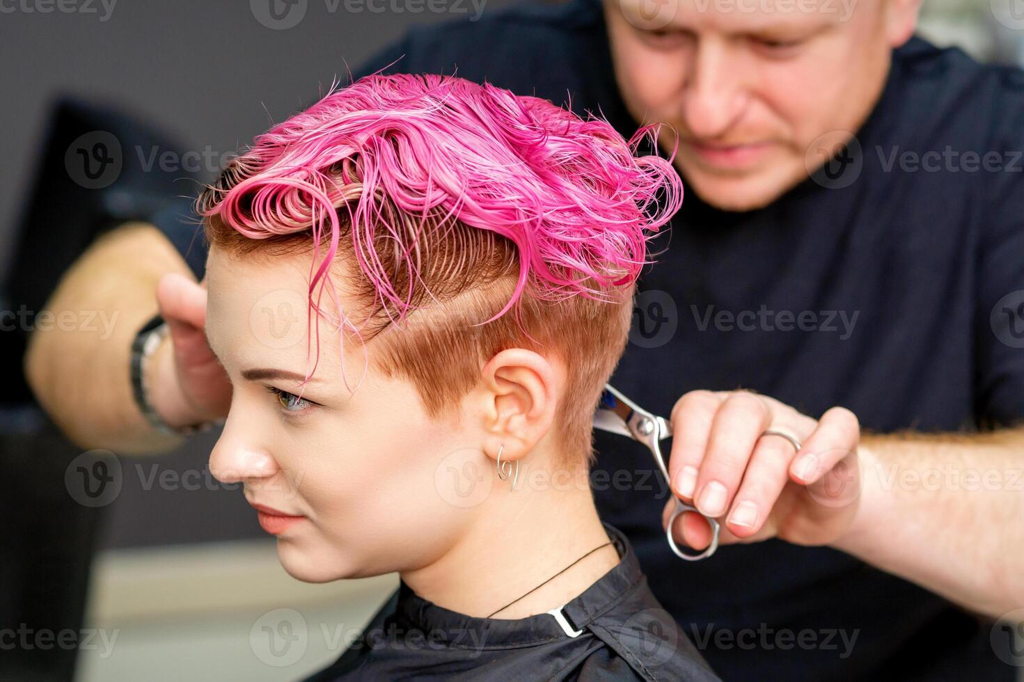 donna avendo un' nuovo taglio di capelli. un' maschio parrucchiere è taglio tinti rosa corto capelli con forbici nel un' capelli salone. foto