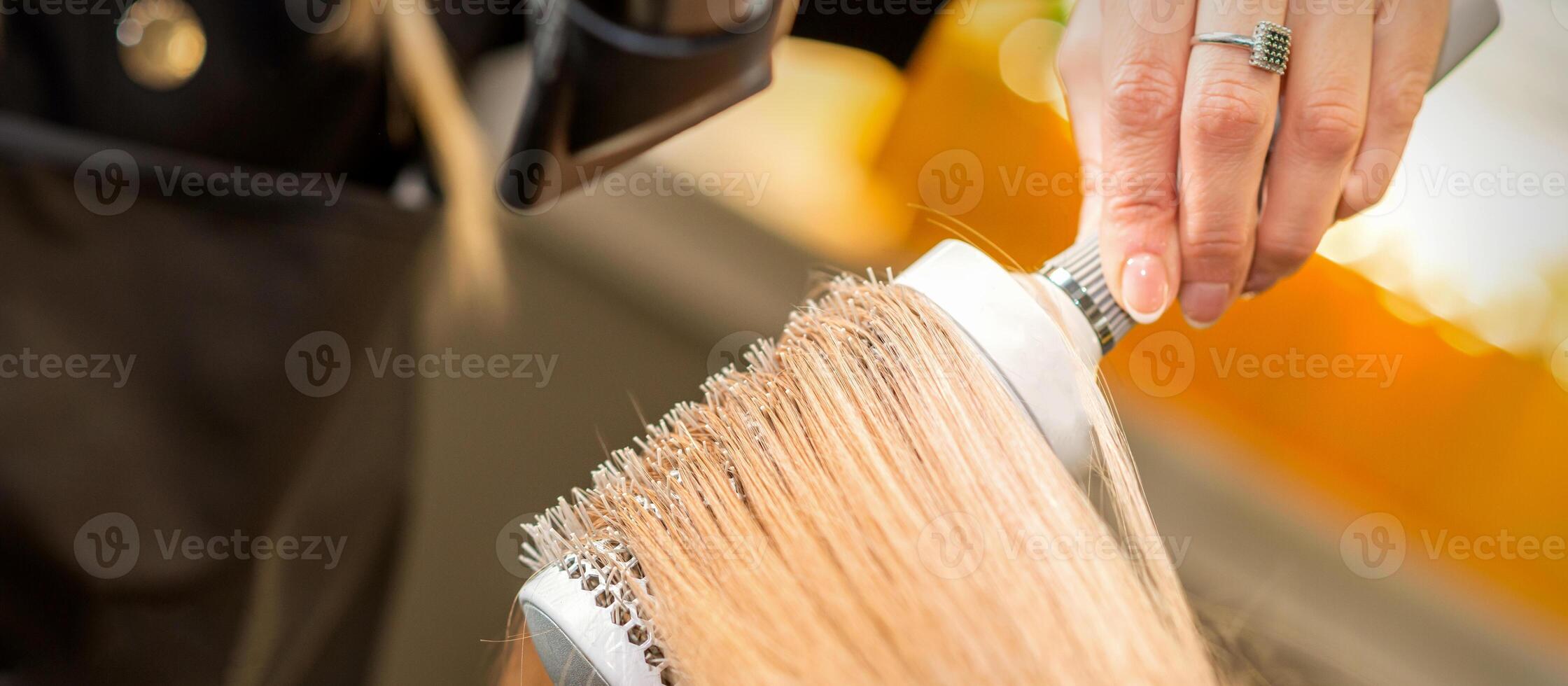 parrucchiere mano essiccazione biondo capelli con un' asciugacapelli e il giro spazzola nel un' bellezza salone. foto