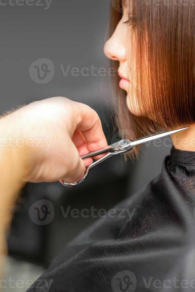 donna avendo un' nuovo taglio di capelli. maschio parrucchiere taglio Marrone capelli con forbici nel un' capelli salone. foto