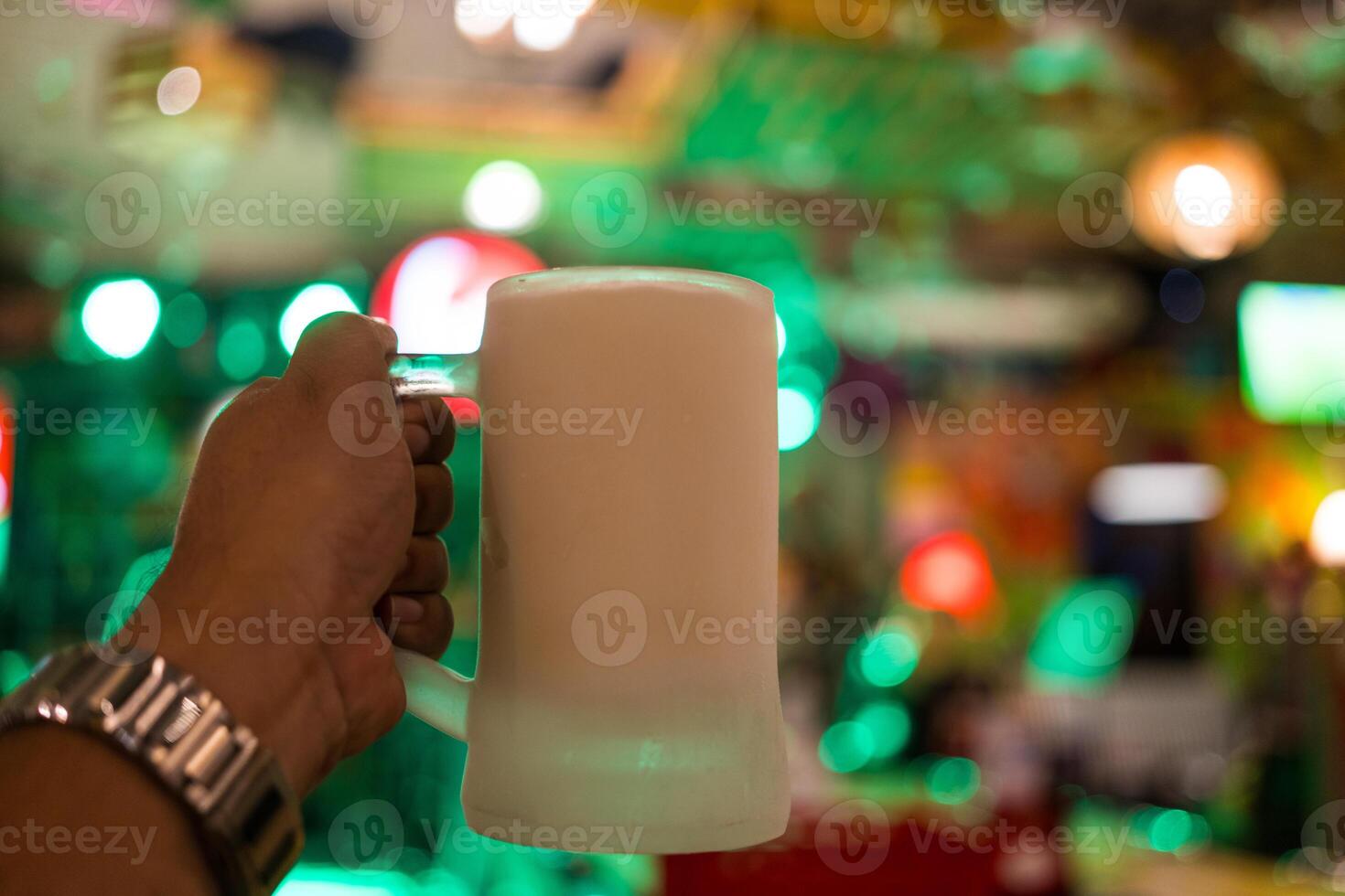 mano Tenere birra nel un' congelato bicchiere con pub leggero sfocatura sfondo foto