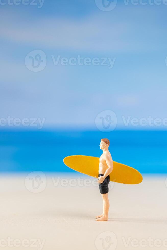 miniatura persone uomo nel un' costume da bagno, e Tenere un' giallo tavola da surf su il spiaggia foto