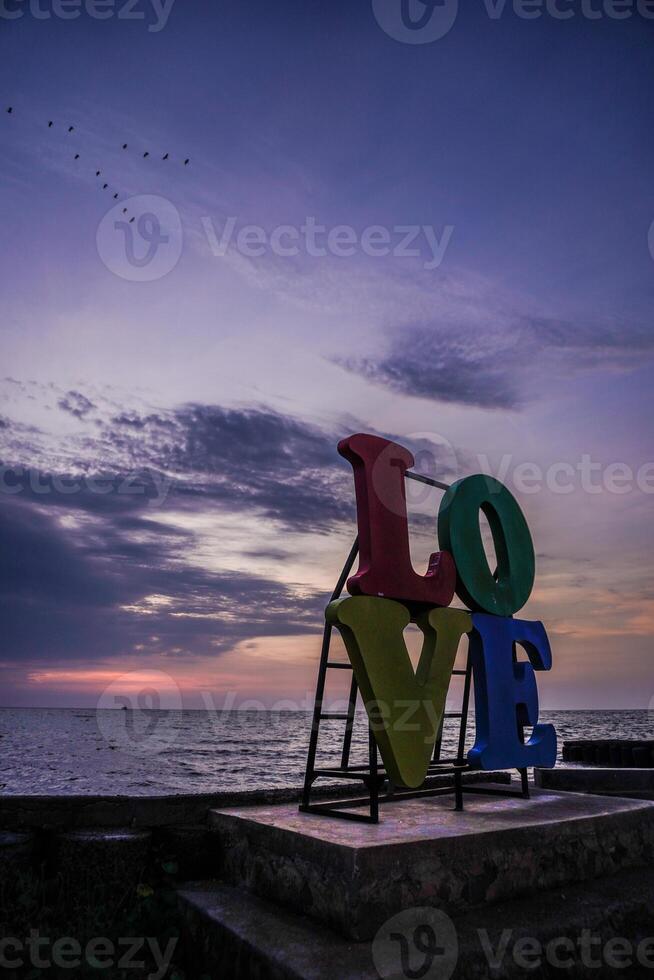 avvicinamento Visualizza di il parola amore posto su il costa contro un' tramonto cielo con vuoto spazio per fotocopiatura. foto