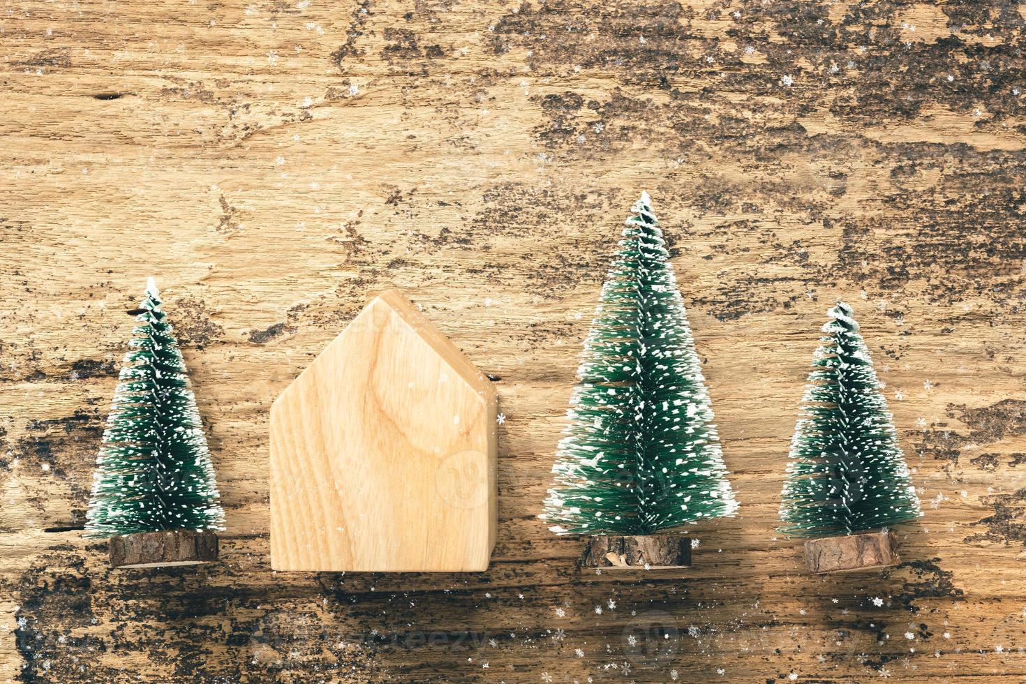 Vista dall'alto del mini giocattolo per la casa in legno dell'albero di Natale su un tavolo in legno rustico con la caduta della neve foto