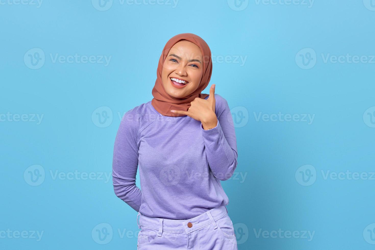 sorridente donna asiatica che mostra chiamami gesto della mano su sfondo blu foto