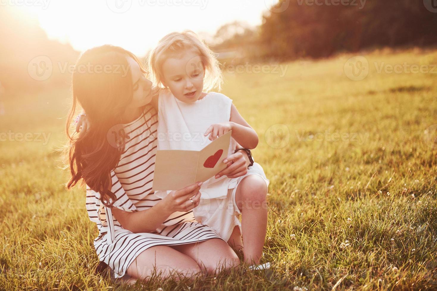 la figlia del bambino si congratula con sua madre e le regala una cartolina. madre e ragazza sorridono e si abbracciano. foto