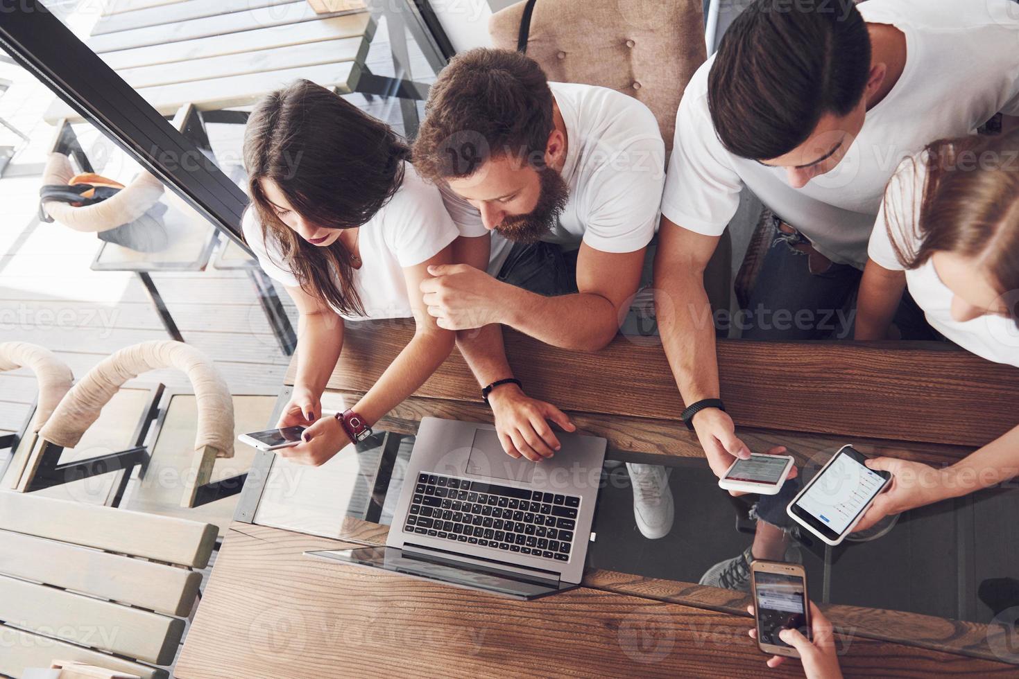 un gruppo di giovani con gadget e un laptop organizza un brainstorming e comunica tra loro. il concetto di sviluppo di un'impresa giovane foto