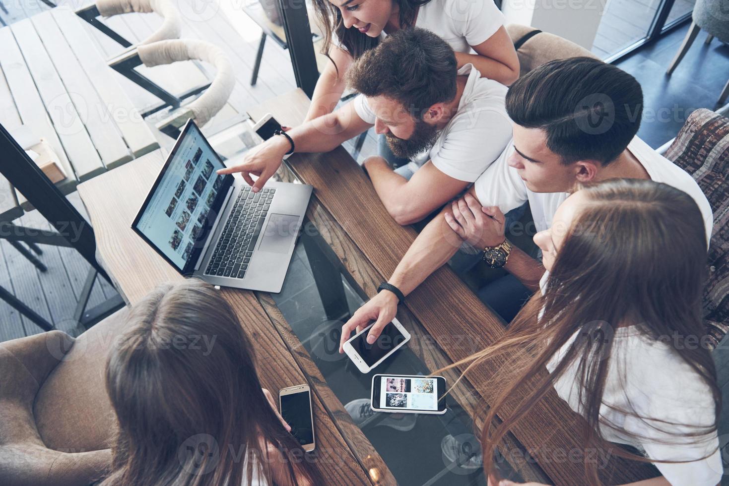 un gruppo di giovani con gadget e un laptop organizza un brainstorming e comunica tra loro. il concetto di sviluppo di un'impresa giovane foto