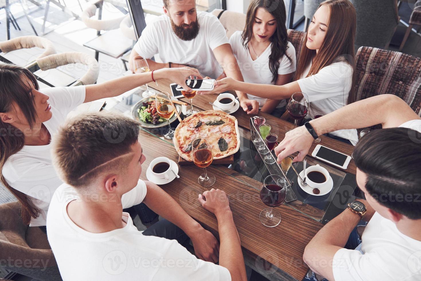 un gruppo di persone fa una foto selfie in un bar. i migliori amici si sono riuniti a tavola mangiando pizza e cantando vari drink