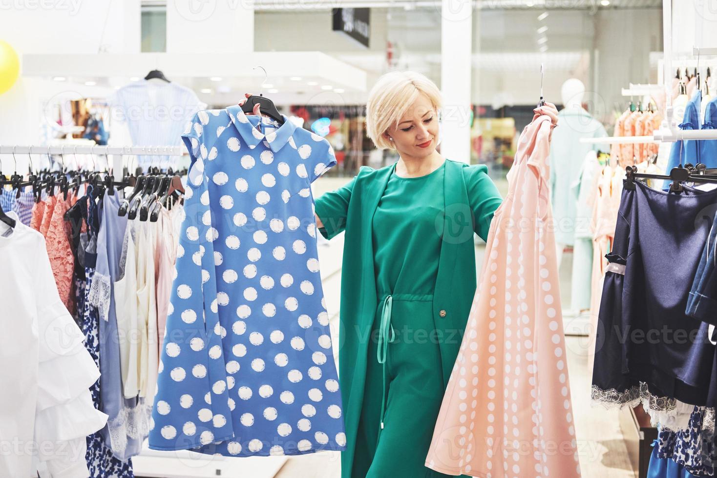 questo vestito è perfetto. la giovane bella donna sorridente fa una scelta quando fa shopping in un negozio foto