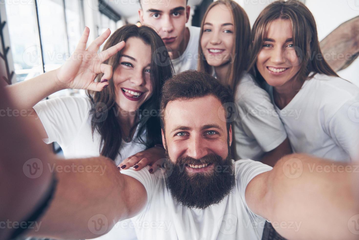 un gruppo di persone fa una foto selfie in un bar. i migliori amici si sono riuniti a tavola mangiando pizza e cantando vari drink