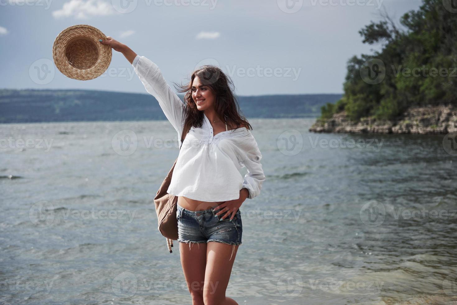 una bella ragazza con un cappello e uno zaino cammina giocosamente sull'acqua. una calda giornata estiva è un ottimo momento per l'avventura e l'avventura nella natura foto