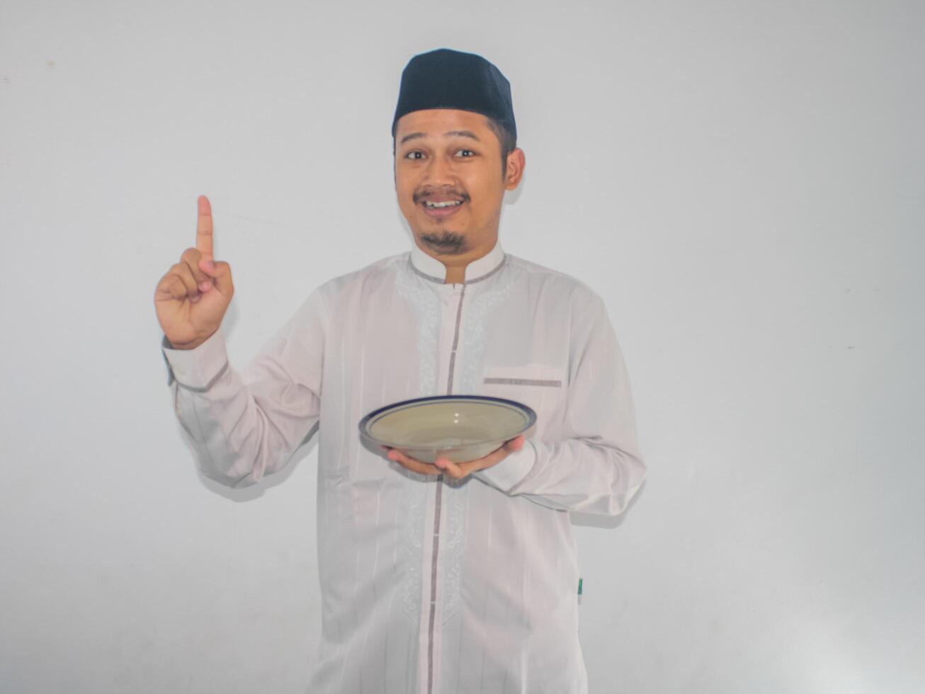 musulmano asiatico uomo sorridente e puntamento per il giusto lato mentre Tenere vuoto cena piatto foto