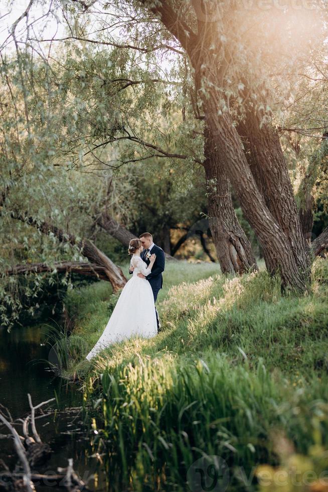 lo sposo e la sposa stanno camminando nella foresta vicino a un fiume stretto foto