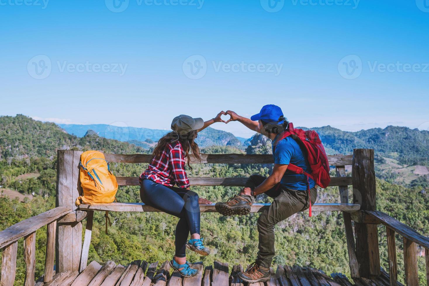 turisti asiatici coppia con zaini felici di viaggiare ha alzato la mano per fare una forma a cuore e godersi il paesaggio naturale sulla montagna. foto