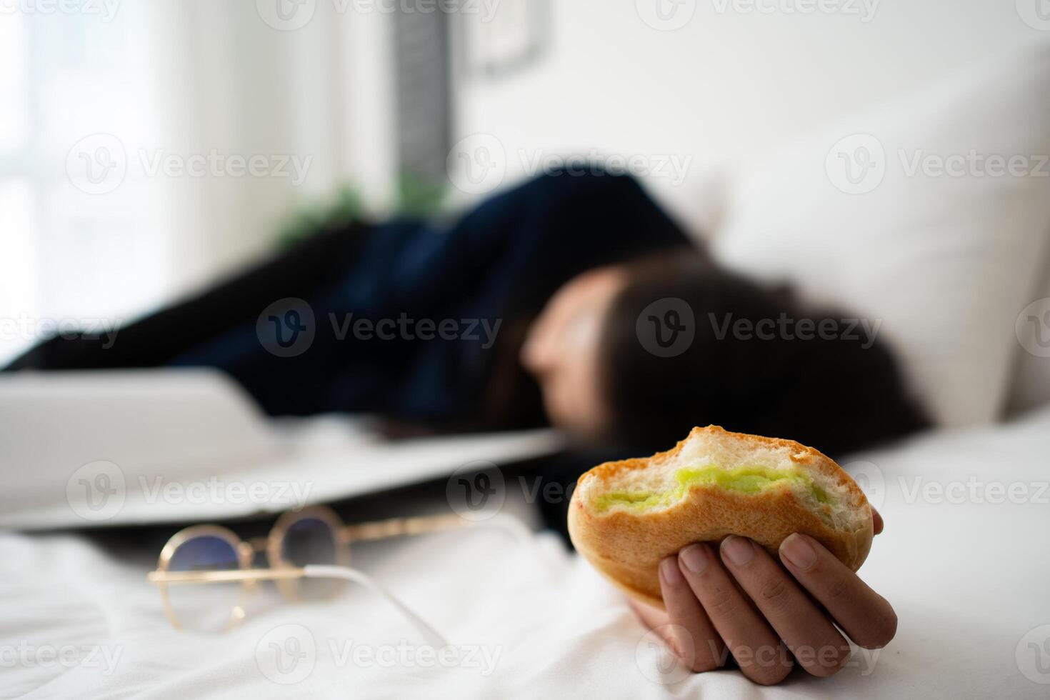 occupato e stanco donna d'affari mangiare pane per prima colazione nel letto a casa e Lavorando per consegnare finanziario dichiarazioni per un' capo. oberati di lavoro e malsano per pronto pasti, bruciato concetto. foto