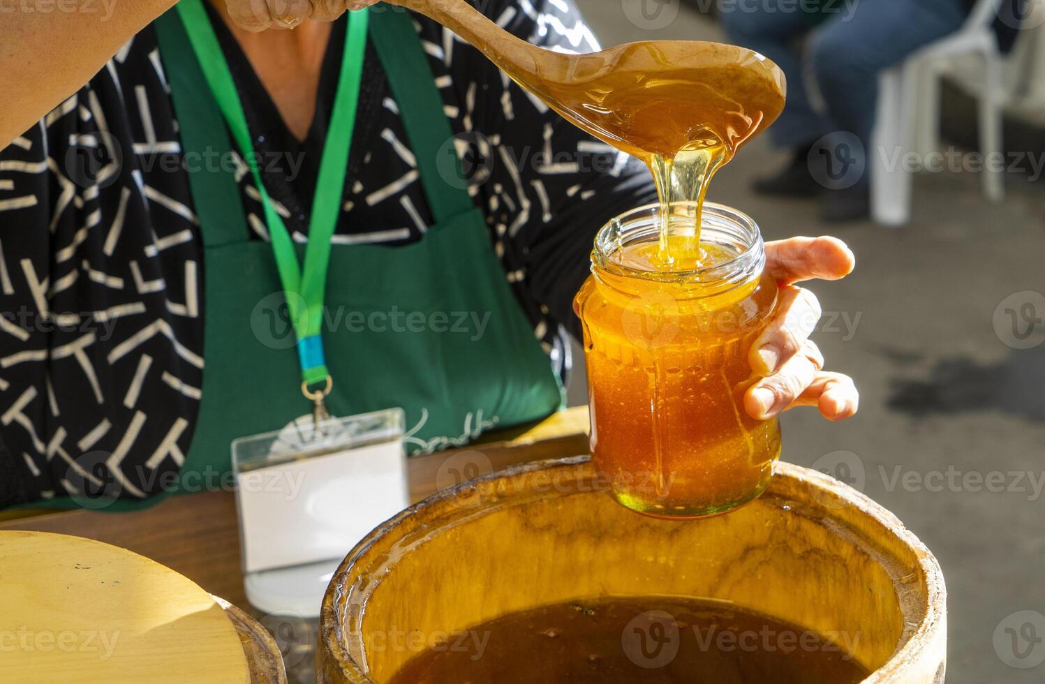 un' donna versa miele a partire dal un' barile in un' bicchiere vaso foto