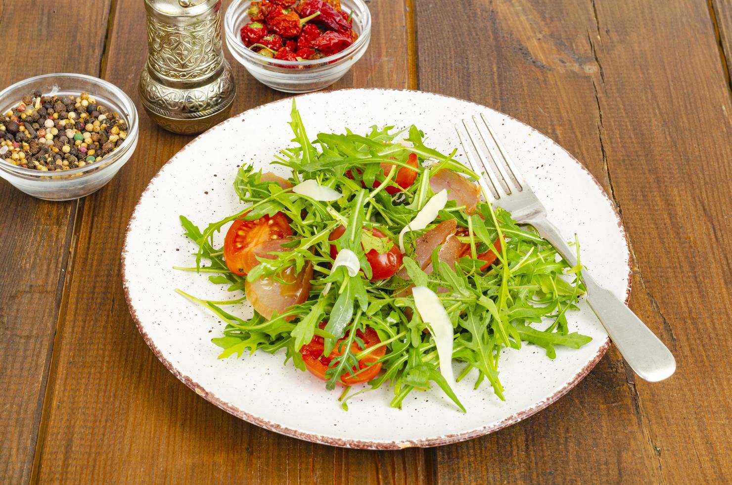 piatto di rucola, pomodori, carne secca e formaggio. insalata su piatto su fondo in legno foto