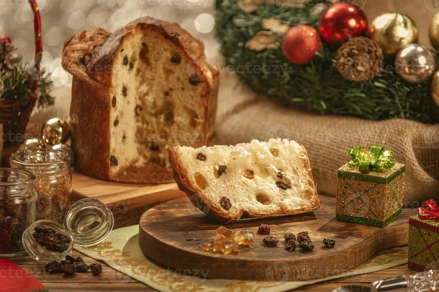 una fetta di panettone e cubetti di frutta candita su un tagliere di legno con addobbi natalizi foto