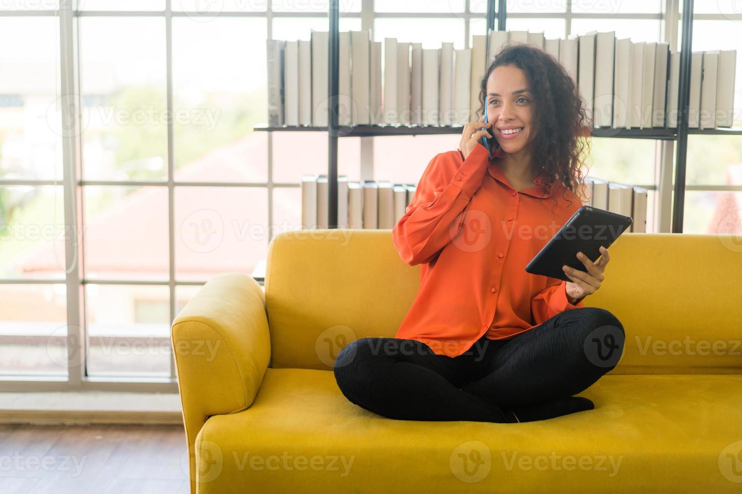 donna latina che utilizza il telefono cellulare o lo smartphone e tiene in mano un tablet foto