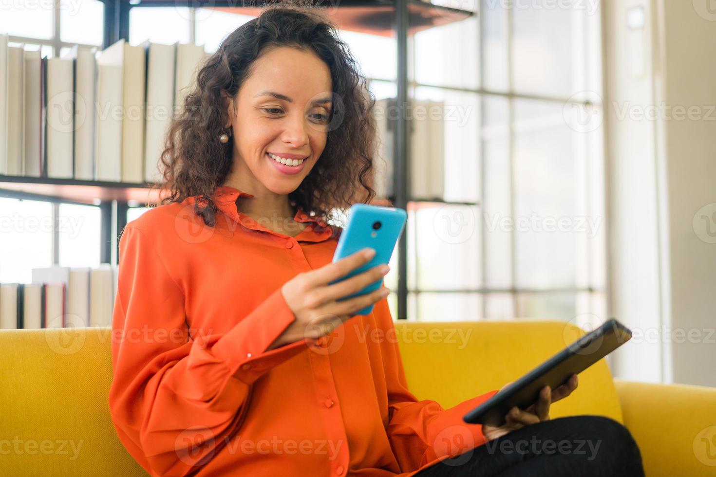 donna latina che utilizza il telefono cellulare o lo smartphone e tiene in mano un tablet foto