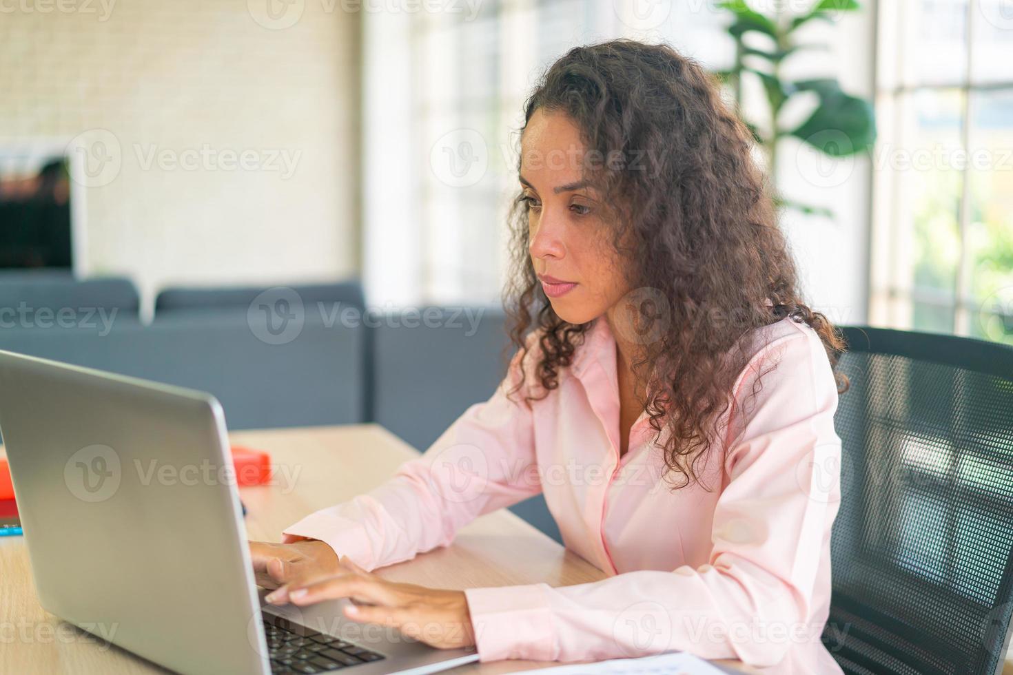 donna latina che lavora con laptop e carta sullo spazio di lavoro foto