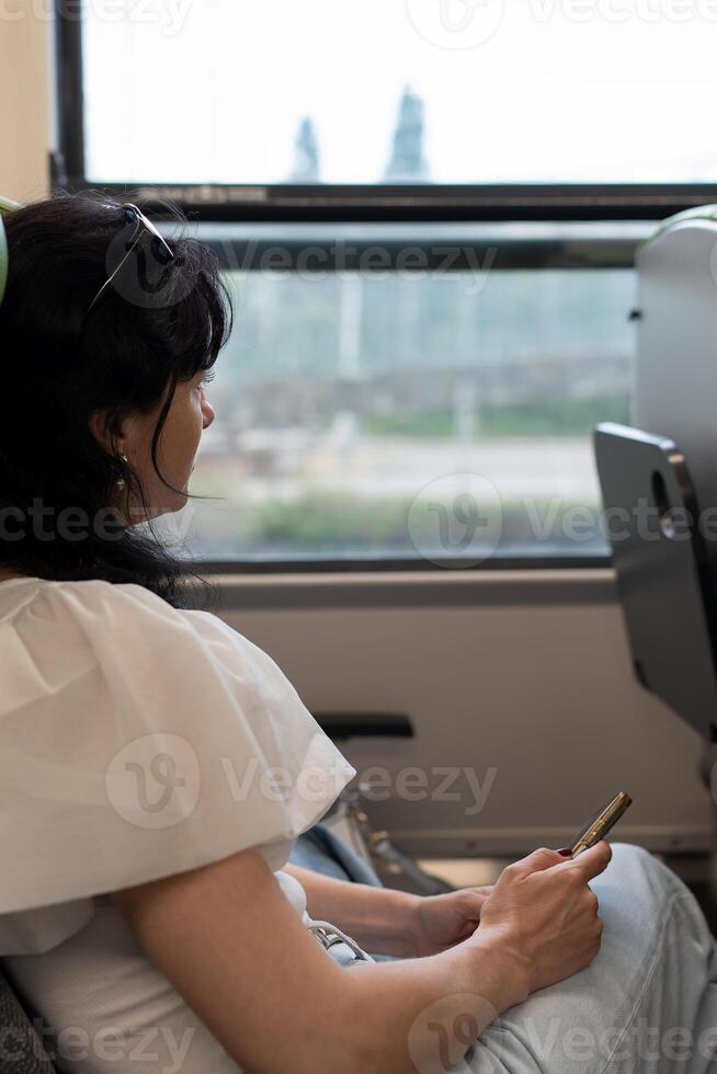 un' seduta ragazza nel trasporto. verticale avvicinamento foto. un' giovane ragazza è seduta su il treno e guardare su il finestra. il concetto di in viaggio di pubblico trasporto. foto