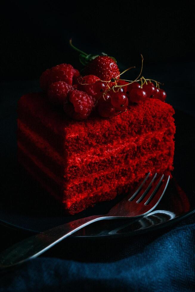 un' pezzo di rosso velluto torta con frutti di bosco su un' nero piatto foto