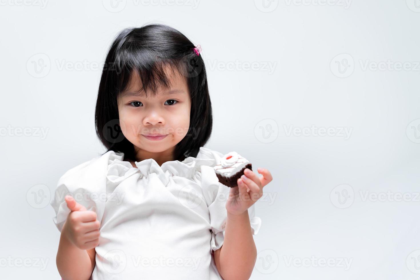 il bambino tiene in mano un piccolo pezzo di torta. la bambina ha dato i pollici in su, il che significa che le caramelle erano deliziose e meravigliose. foto