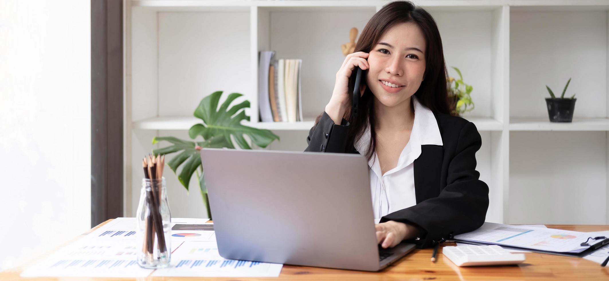 donna asiatica d'affari che utilizza smartphone per fare finanza matematica sulla scrivania di legno in ufficio, tasse, contabilità, concetto finanziario foto