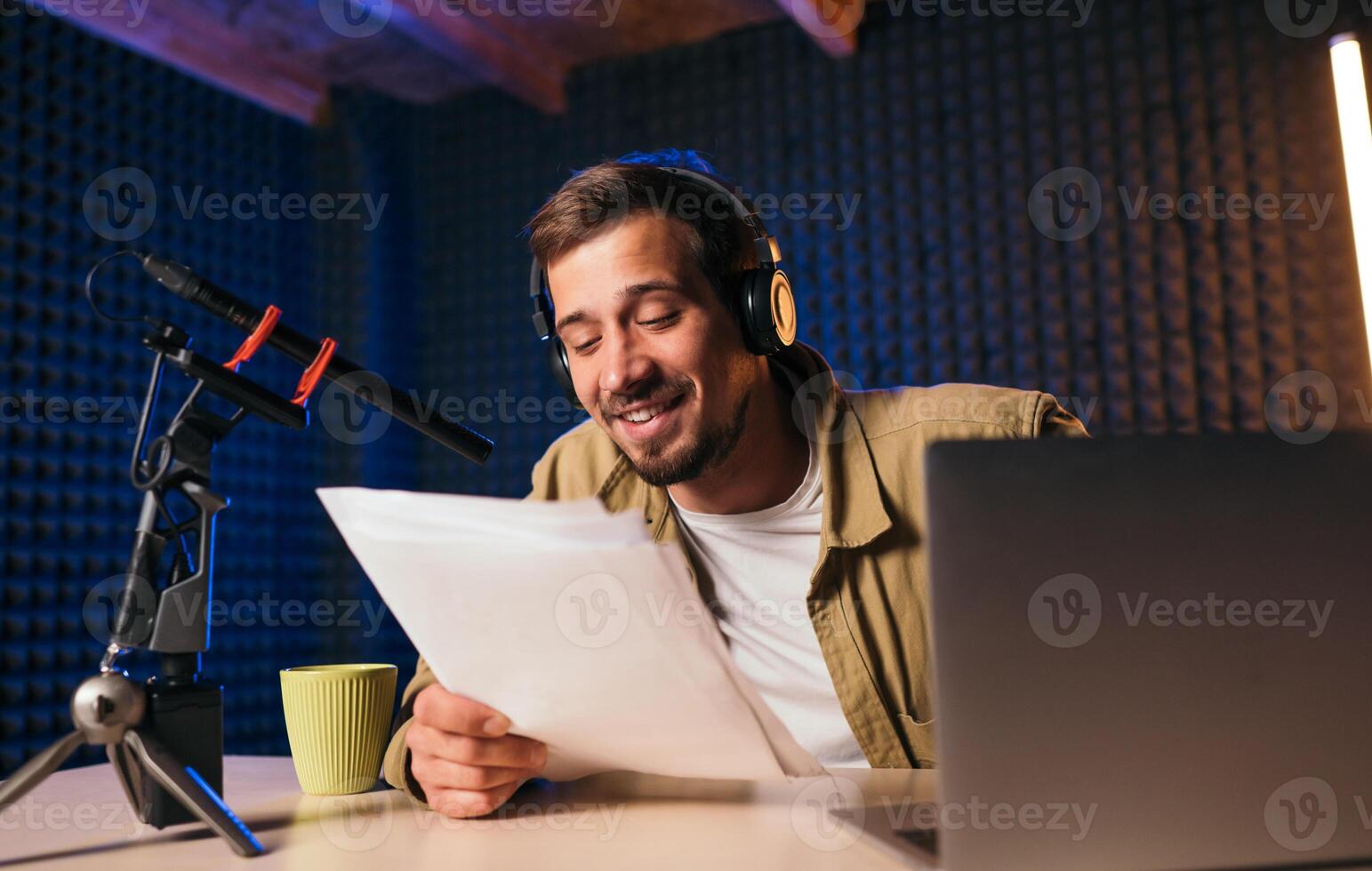 sorridente Radio ospite con cuffie lettura notizia a partire dal carta in studio microfono a Radio stazione con neon luci. guardare a telecamera foto