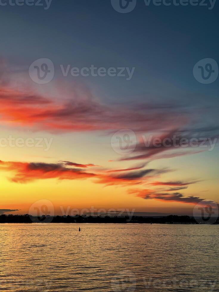 mozzafiato tramonto pittura il cielo con occhiali da sole di rosso e arancia, riflessa sottilmente su il acqua per un' Perfetto tranquillo, calmo sera ambiance foto