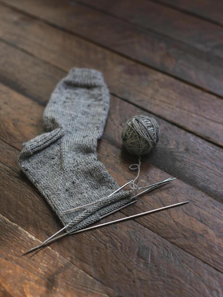 mano a maglia calzino con aghi e grigio filato palla su buio di legno sfondo. foto