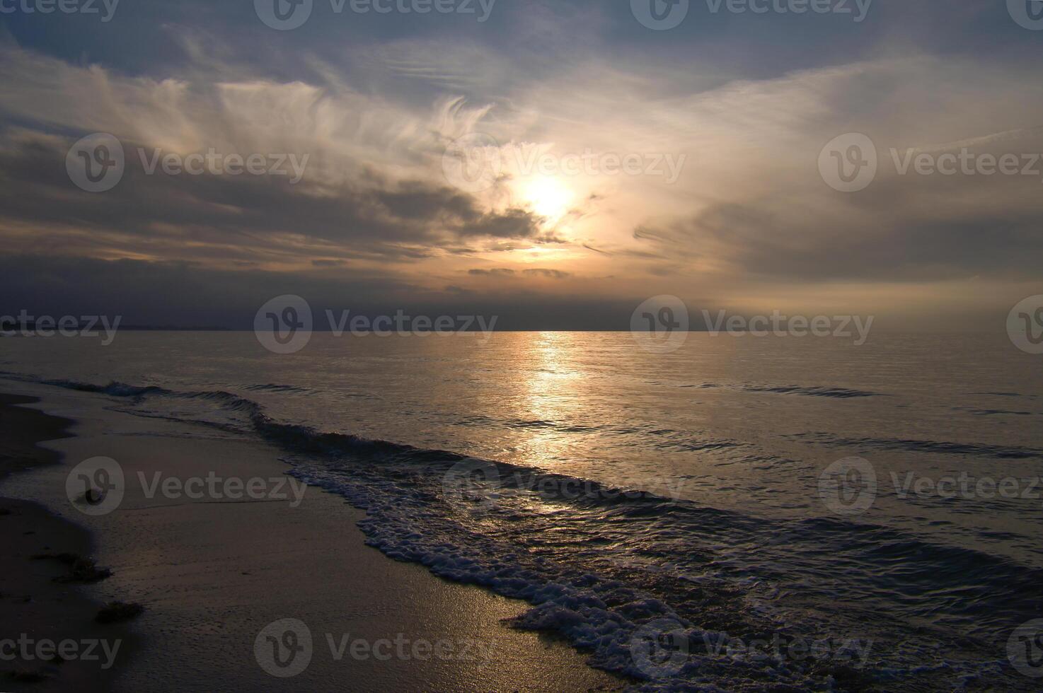 tramonto, illuminato mare. sabbioso spiaggia nel il primo piano. leggero onde. baltico mare foto