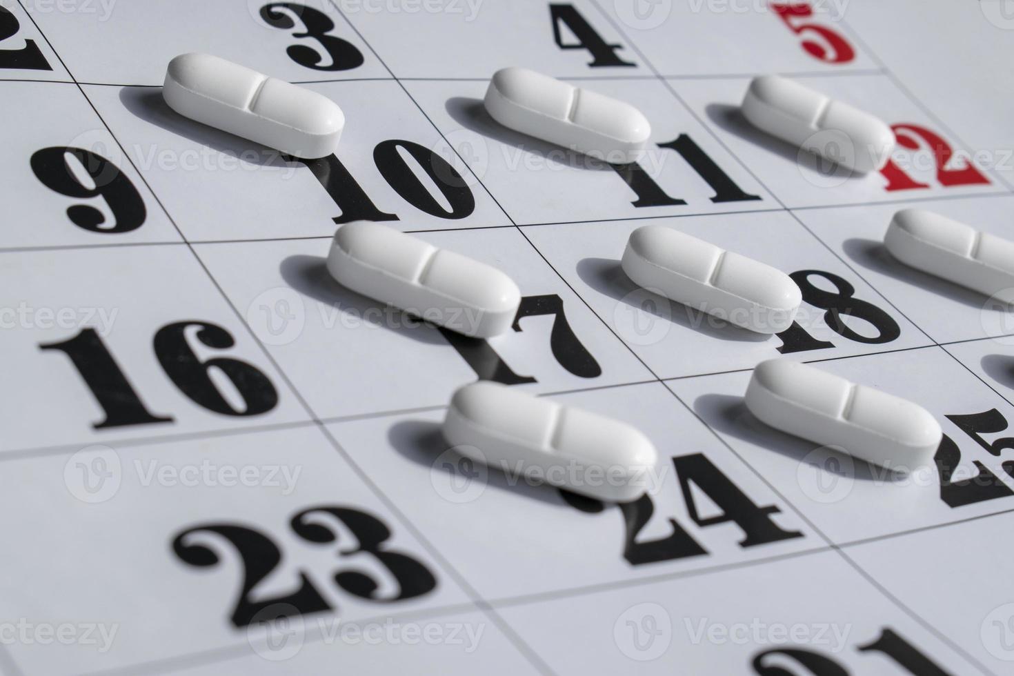 primo piano di pillole bianche su un calendario. piano farmacologico, programma, elenco o concetto di calendario. foto