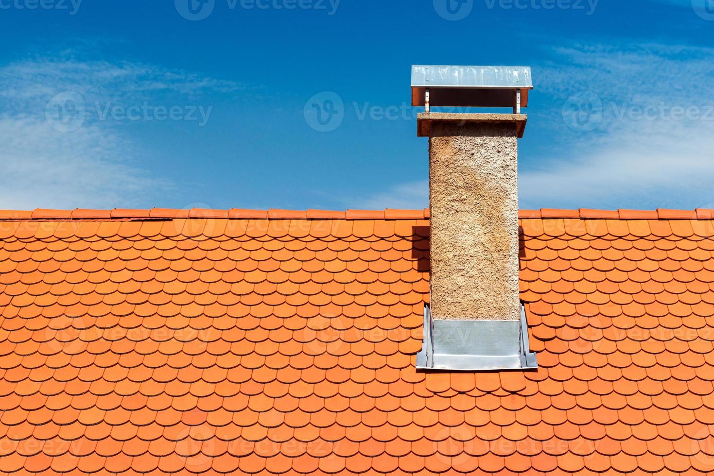 tetto moderno con camino. piastrelle di ceramica arancione, scandole. cielo azzurro sullo sfondo foto