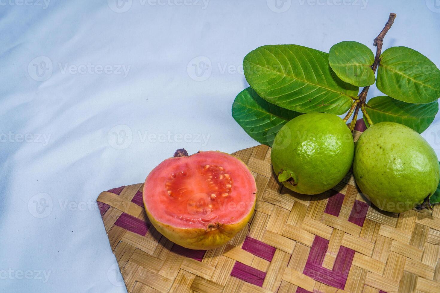 guaiava isolato. collezione di rosso incarnato guaiava frutta con giallastro verde pelle e le foglie isolato su un' bianca sfondo con bambù stuoia. foto