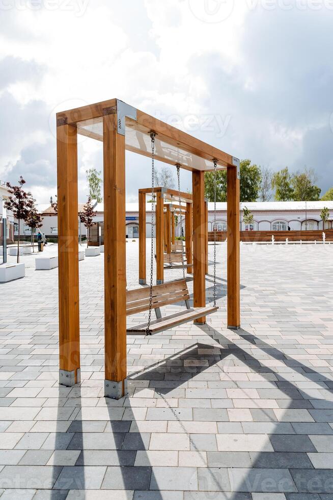 di legno altalene nel il città parco, un' panchina sospeso su Catene, un' posto a sedere per riposo, un' posto per a passeggio, un arte oggetto, moderno design. foto