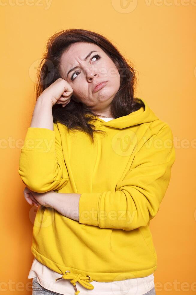 caucasico donna con un' acuto immaginazione e domande nel mente. femmina persona indossare un' maglione ha contemplativo espressione su telecamera, mano riposo su fronte, pensiero di un idea. foto