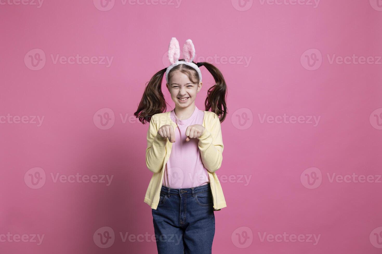 adorabile poco ragazza la spesa Pasqua vacanza di Hopping in giro piace un' coniglio per il telecamera mentre indossare coniglietto orecchie. Contentissimo contento giovanotto giocando e ridacchiando su rosa sfondo. foto