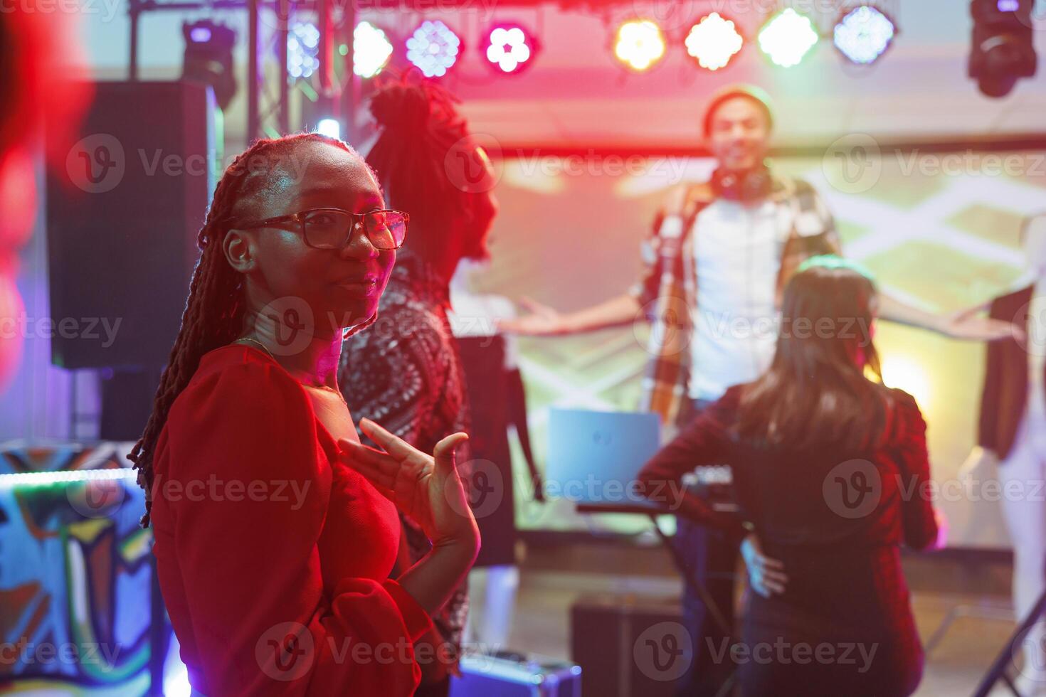africano americano donna in piedi su pista da ballo mostrando con mano a se stessa nel discoteca. giovane clubber avendo divertimento, rilassante e partying nel club con faretti, godendo vita notturna foto