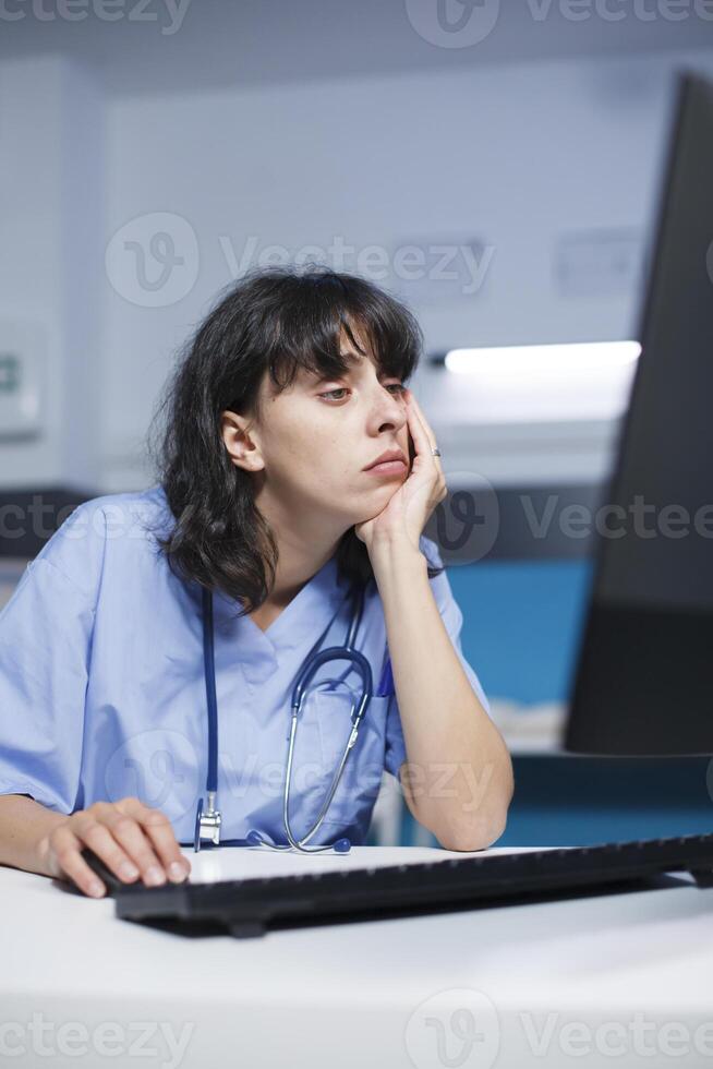 caucasico femmina professionista a un' moderno clinica scrivania, stanco ma focalizzata. prima un appuntamento, farmacista allenato infermiera analisi un' medico verifica utilizzando computer nel il ospedale ufficio. foto