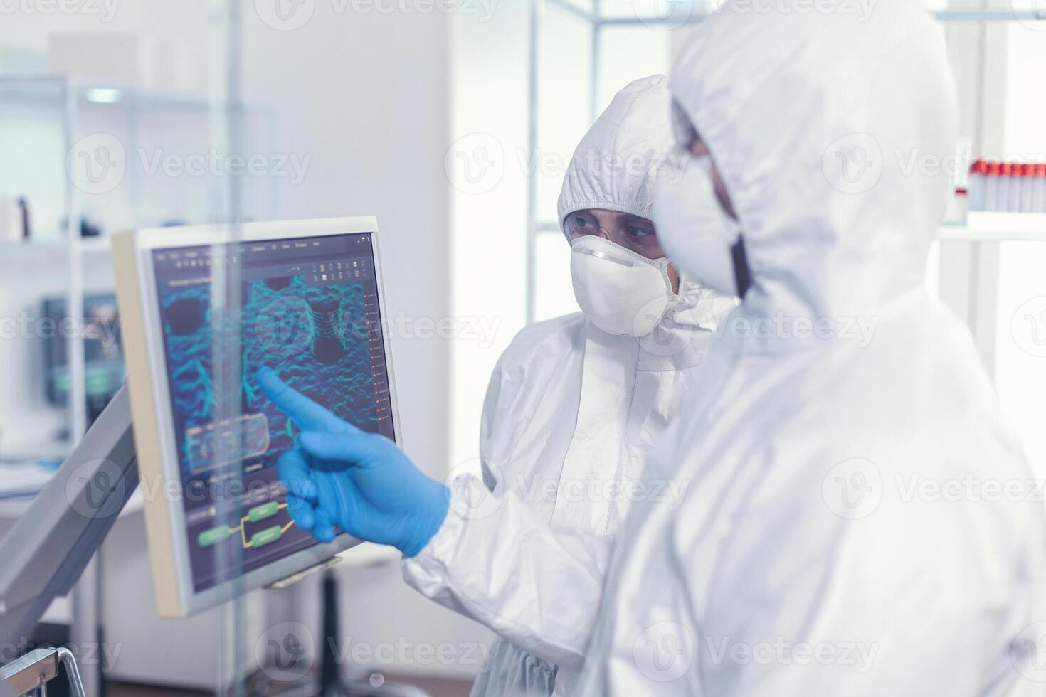 chimico nel ppe completo da uomo spiegare per medico vaccino sviluppo nel moderno attrezzata laboratorio puntamento su computer desktop. medici l'esame virus Evoluzione utilizzando alto Tech ricercando diagnosi contro covid19 foto