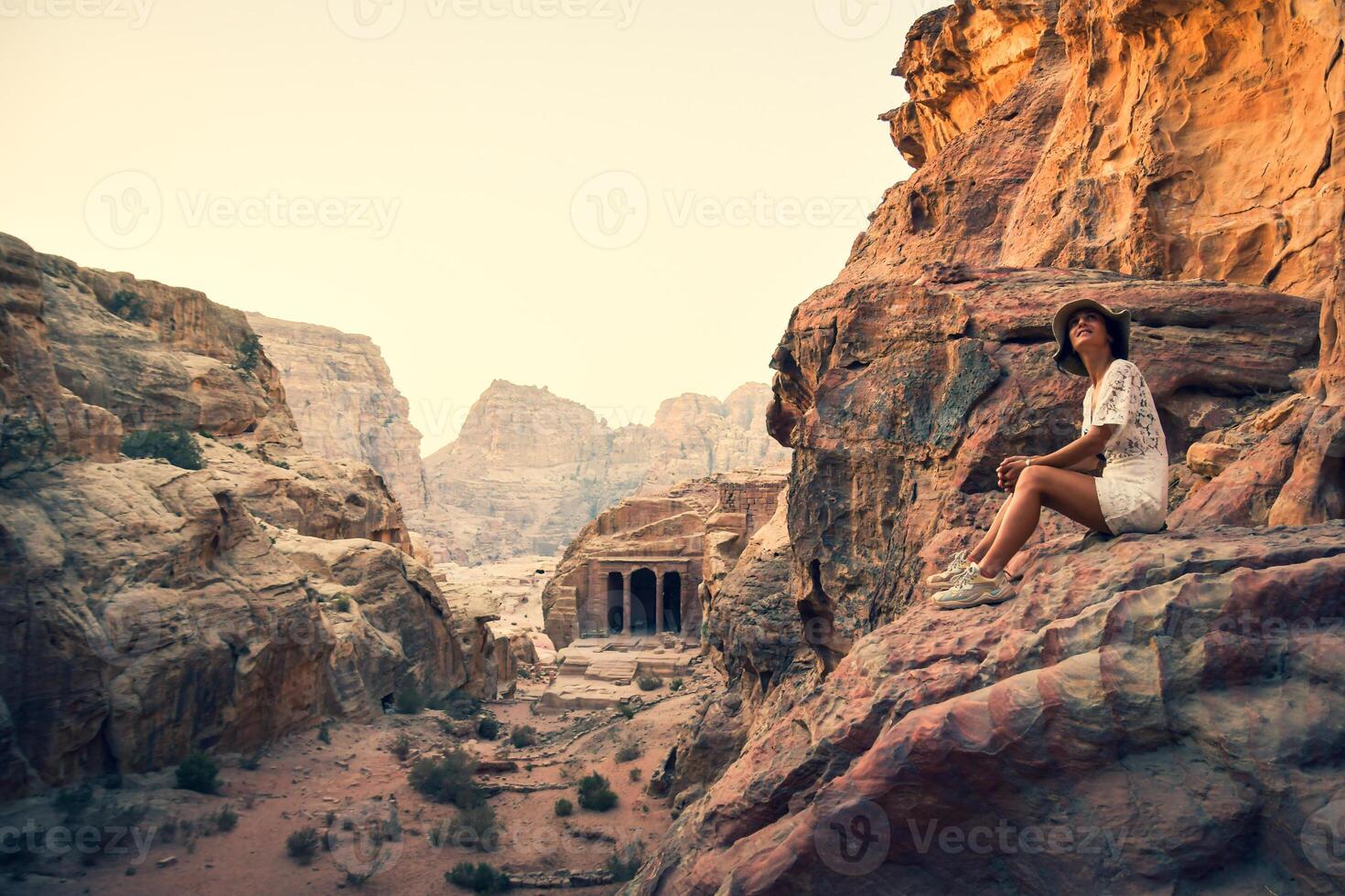 caucasico giovane femmina turista sedersi e Sorridi mentre guardare per bellissimo petra antico città intagli. famoso visitare Giordania attrazione destinazione. petra archeologico luogo panorama foto