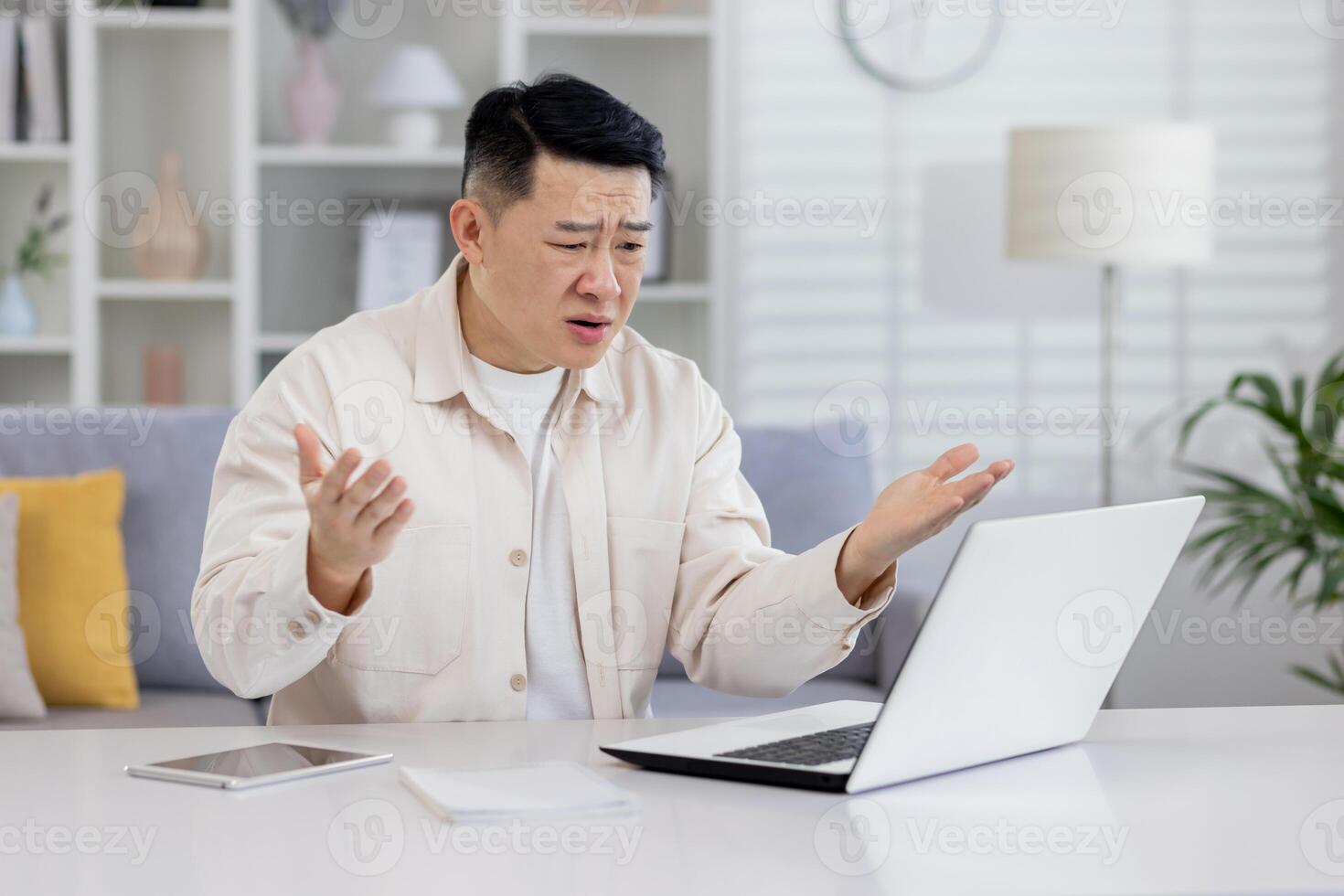 arrabbiato uomo a casa Lavorando con computer portatile, frustrato asiatico uomo guardare a il computer portatile schermo avuto cattivo notizia e insoddisfacente opera risultato, libero professionista Lavorando dentro casa ufficio. foto