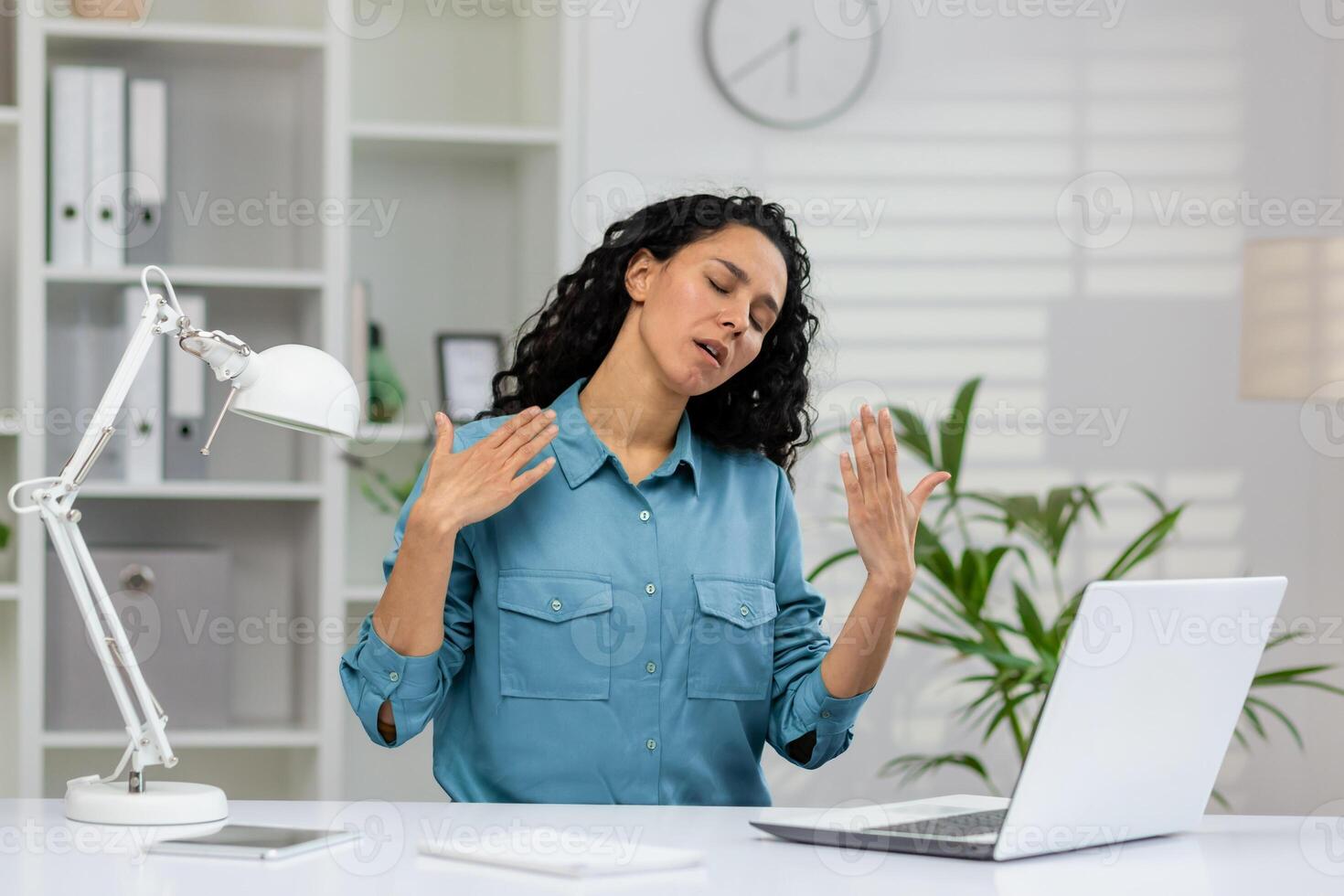 un oberati di lavoro donna d'affari è ventaglio se stessa, mostrando segni di calore e disagio nel un' brillantemente illuminato ufficio ambientazione. foto