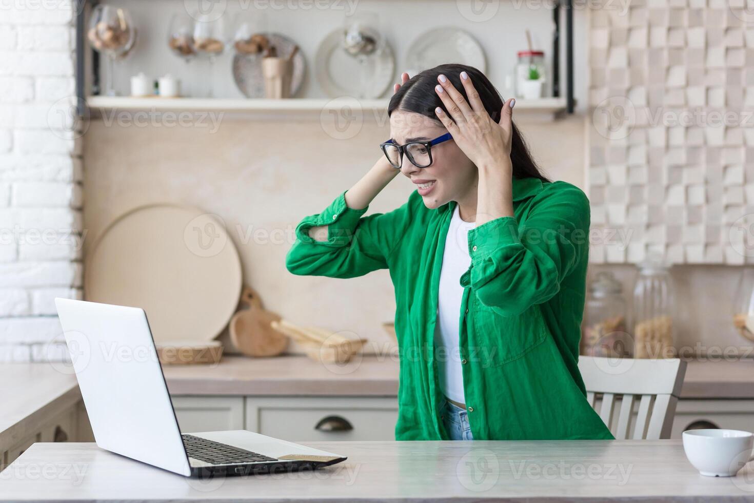 stressato donna a casa Lavorando nel cucina utilizzando computer portatile, avuto cattivo notizia in linea foto