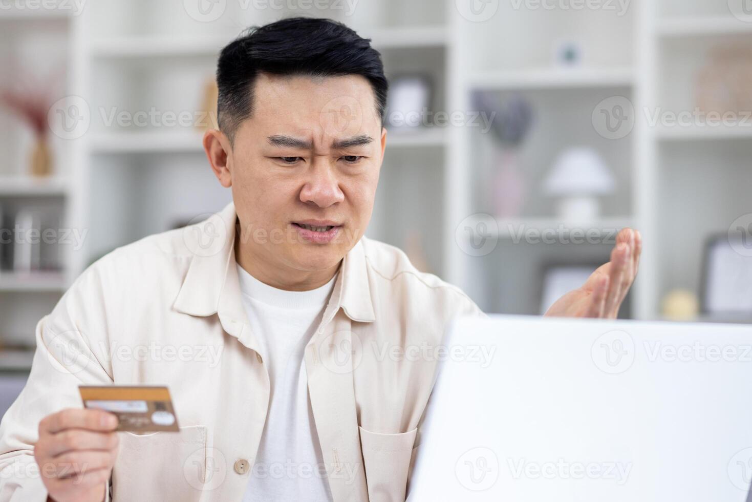 asiatico uomo imbrogliato di truffatori, uomo seduta a casa a tavolo Tenere banca credito carta, respinto i soldi trasferimento, negativo account equilibrio, irritato e deluso. foto